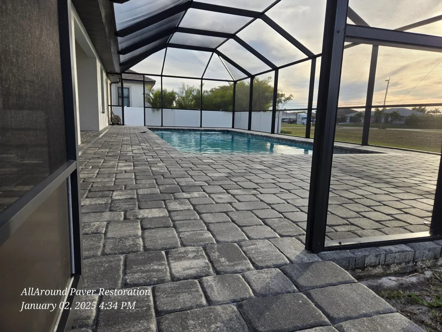 Sealed cobblestone paver pool deck at dusk inside a Cape Coral screen enclosure